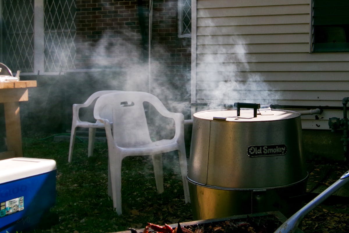 Backyard barbecue smoker with smoke rising beside patio chairs on a summer afternoon